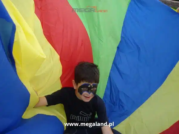 Chłopiec w masce bawi się kolorowym spadochronem.