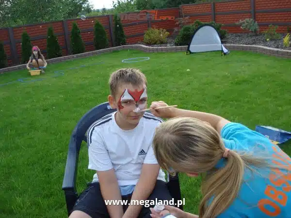 Dziecko z malowaną twarzą na przyjęciu w ogrodzie.