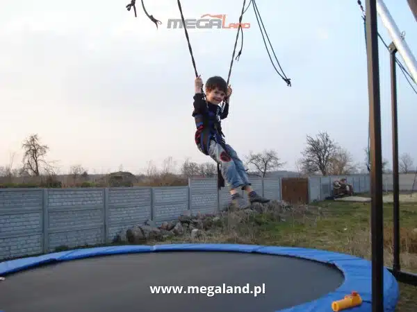 Chłopiec skacze na trampolinie na zewnątrz.