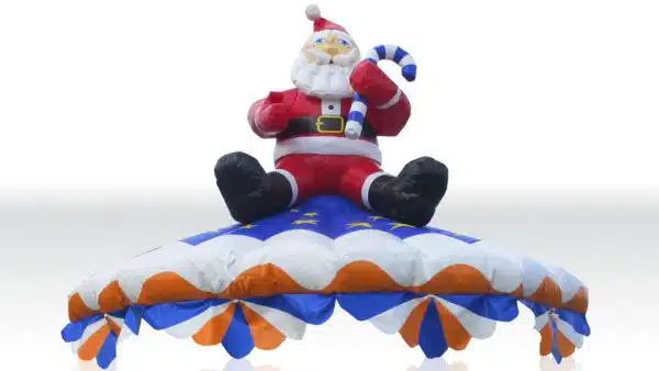 Karuzela Mikołaj w Megaland - wesoły Święty Mikołaj siedzący na barwnej, dmuchanej karuzeli, z lśniącą, błękitno-pomarańczową parasolką zdobioną gwiazdami, idealna atrakcja na świąteczny festyn.
