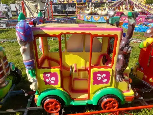 Wagon Kolejki Elektrycznej od Megaland - żywy żółty autobus, który zaprasza młodych pasażerów na barwną podróż przez świat fantazji i rozrywki." Nazwa pliku: Kolejka_Elektryczna_Całość_Megaland