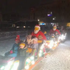 Świąteczna kolejka Megaland z postaciami Mikołajów oświetlona kolorowymi światłami, tworząca radosną atmosferę zimowych festynów i imprez.
