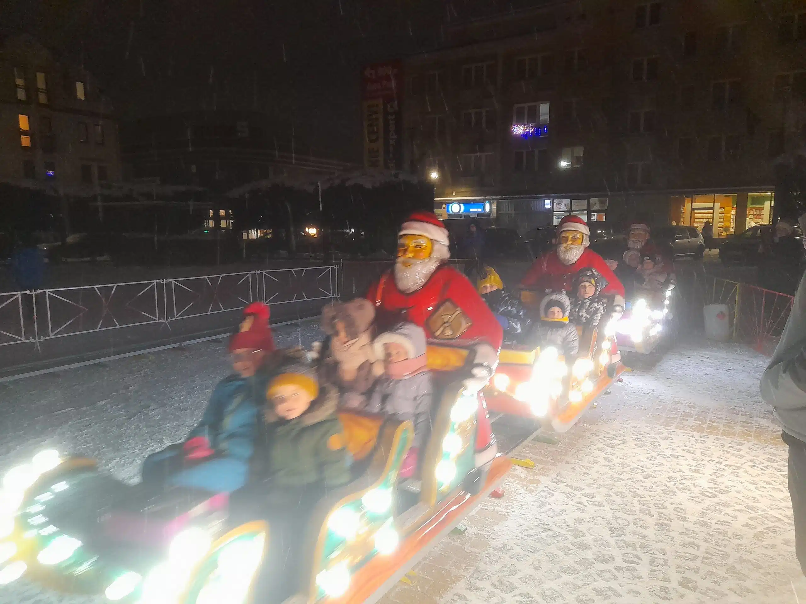 Świąteczna kolejka Megaland z postaciami Mikołajów oświetlona kolorowymi światłami, tworząca radosną atmosferę zimowych festynów i imprez.